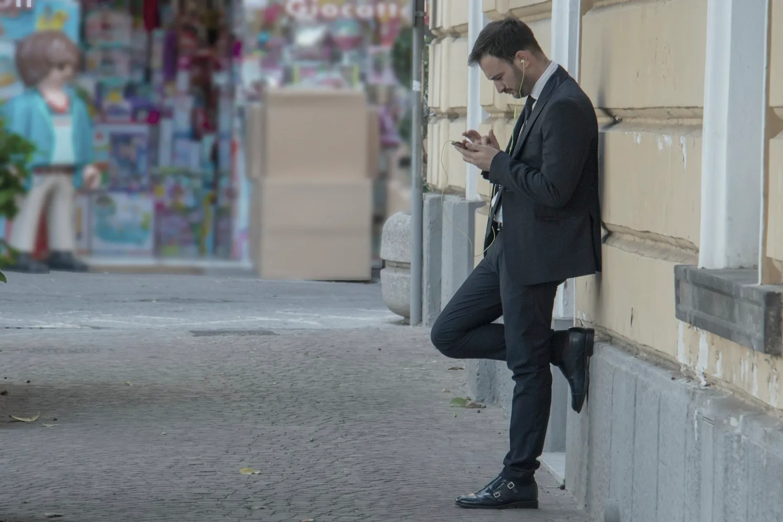 A man in a suit leaning against a building, reading his phone